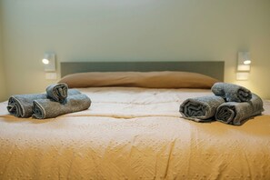 Ein ordentlich bezogenes Bett mit aufgerollten Handtüchern, einem Kopfteil und Wandleuchten.