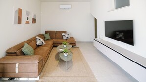 En moderne stue med en hjørnesofa, et sofabord med planter, et fladskærms-tv ophængt på væggen og kunst på væggen.