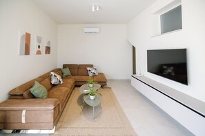 Ein modernes Wohnzimmer mit einer Eckcouch, einem Couchtisch mit Pflanzen, einem flachbildfernseher an der Wand und Bildern an der Wand.