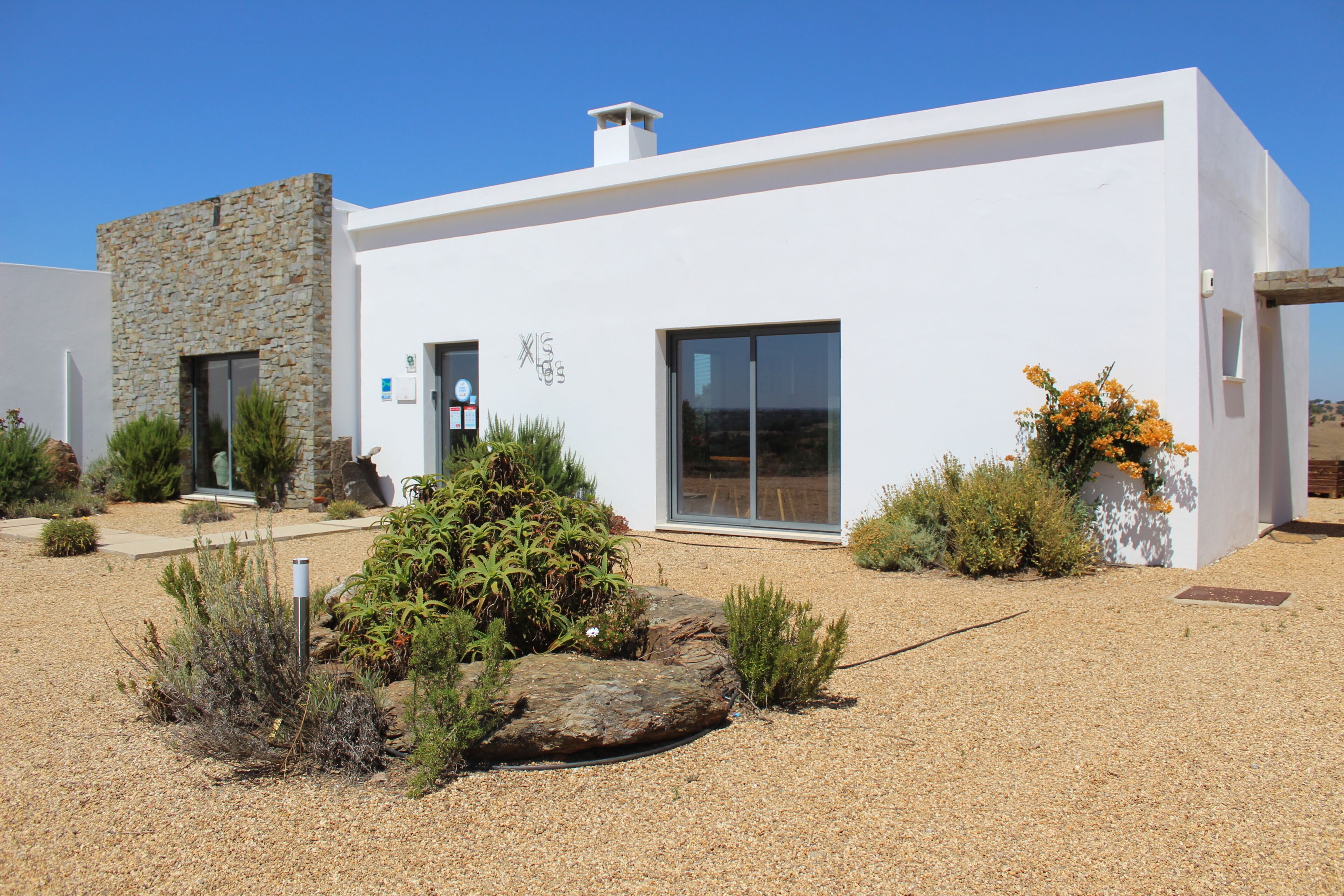 Un edificio moderno con fachada de piedra, grandes ventanales y un jardín bien cuidado con rocas y plantas.