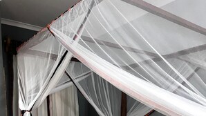 Una cama con estructura de madera, ropa de cama blanca y mosquitero.