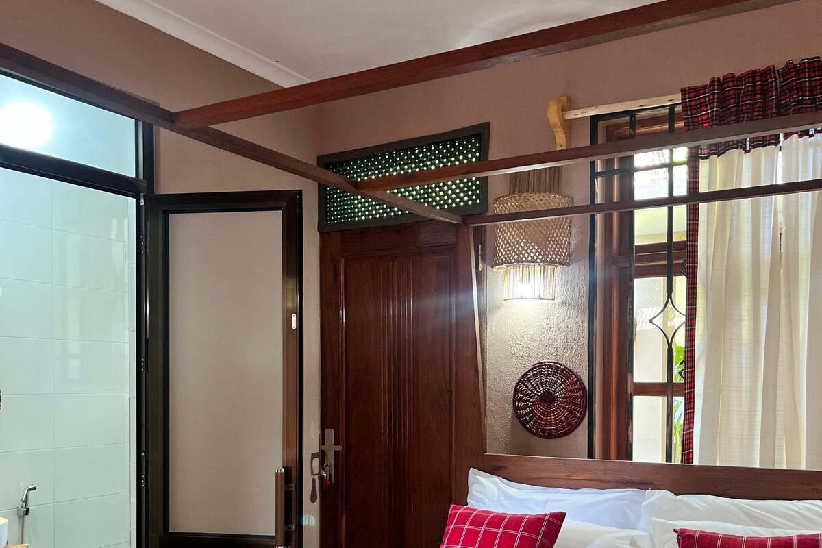 A hotel room with a bed, a wooden headboard, a window with curtains, a door, and a shower area.