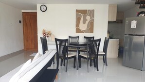 Un comedor con una mesa y sillas, un reloj en la pared y una cocina al fondo.