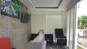 Un espacio de oficina moderno con una mesa larga, dos sillas negras, una silla roja, un ventanal con persianas y una pantalla montada en la pared.
