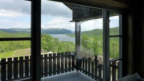 A room with a large window overlooking a lake and forested hills. - 360-degree views from a mountain top in Numedal (Rødberg)