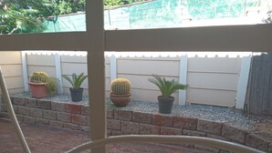 A patio with potted plants, a brick wall, and a white fence. - Self-Catering Accommodation in Suiderhof, Windhoek (Windhoek)