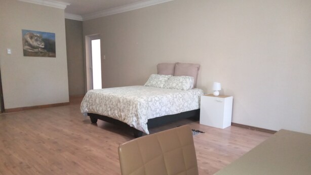 A bedroom with a bed, a nightstand, a chair, and a door. - Self-Catering Accommodation in Suiderhof, Windhoek (Windhoek)