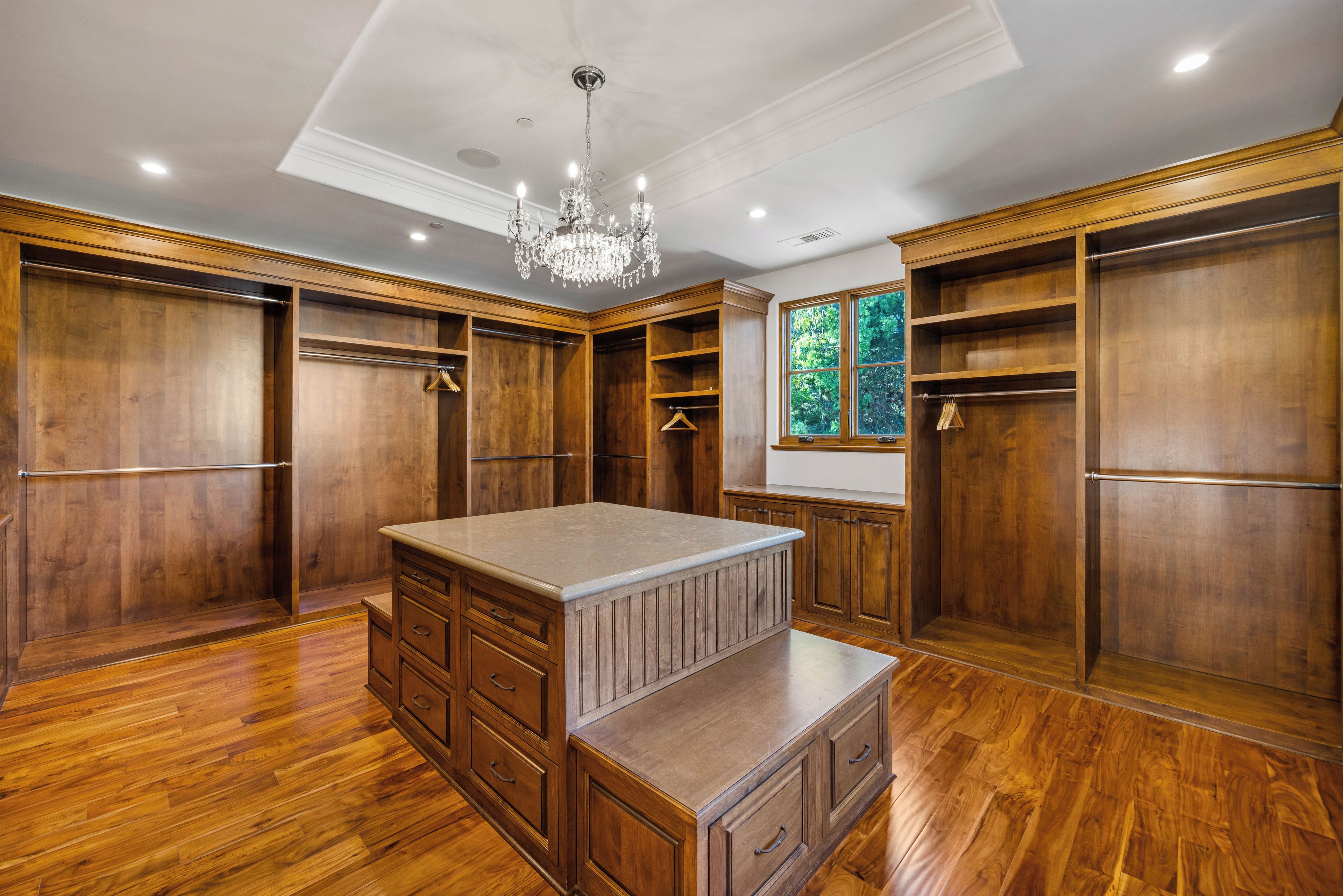 Une pièce spacieuse avec une grande armoire en bois, un îlot central doté de tiroirs et un lustre.