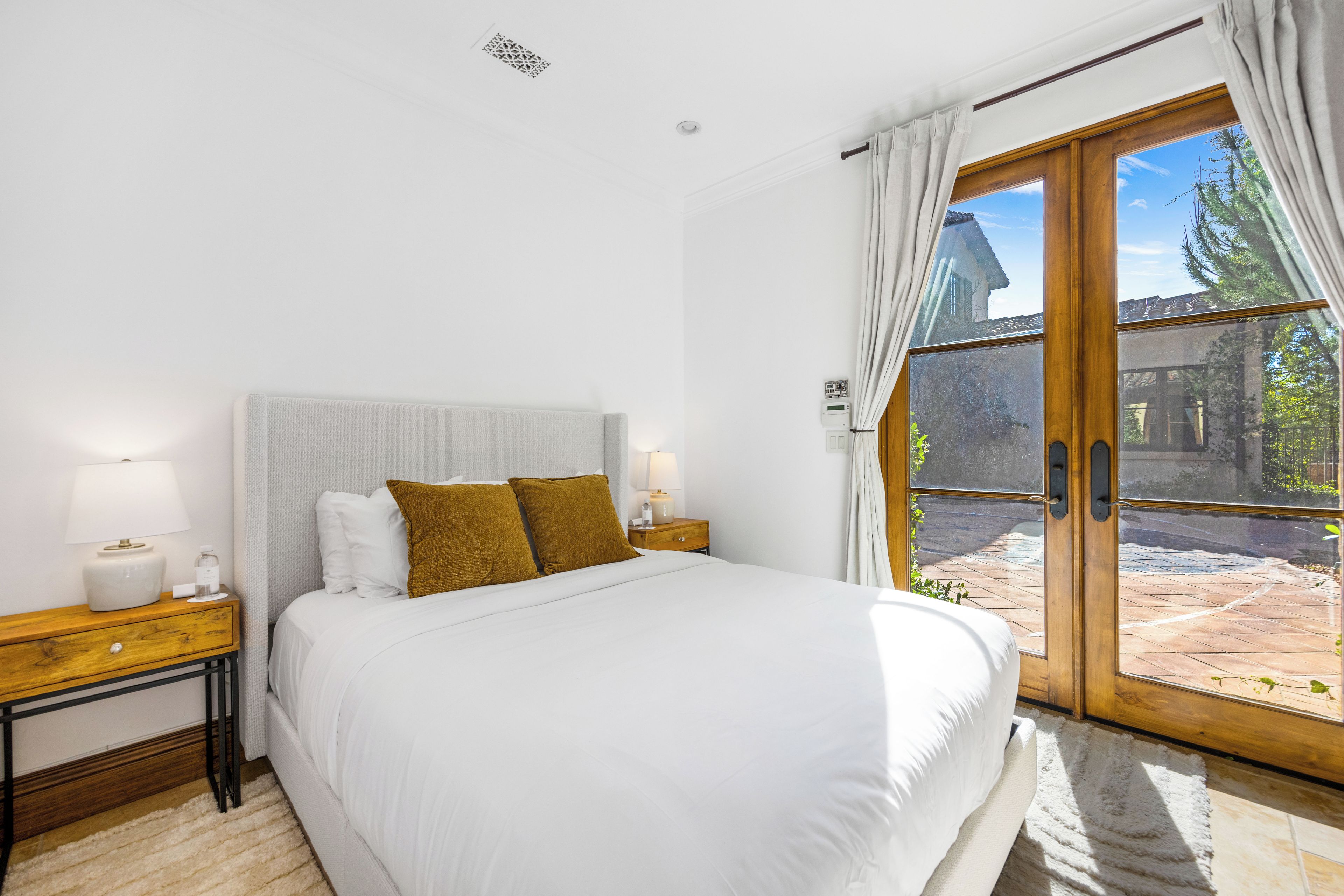 Une chambre à coucher avec un lit, des tables de chevet, une lampe, un thermostat et une vue sur l’extérieur.