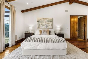 A bedroom with a large bed, two bedside tables, a painting, and a wooden door. - Bel Air Panorama - Mediterranean Estate w/ Resort-Style Grounds (Bel Air)