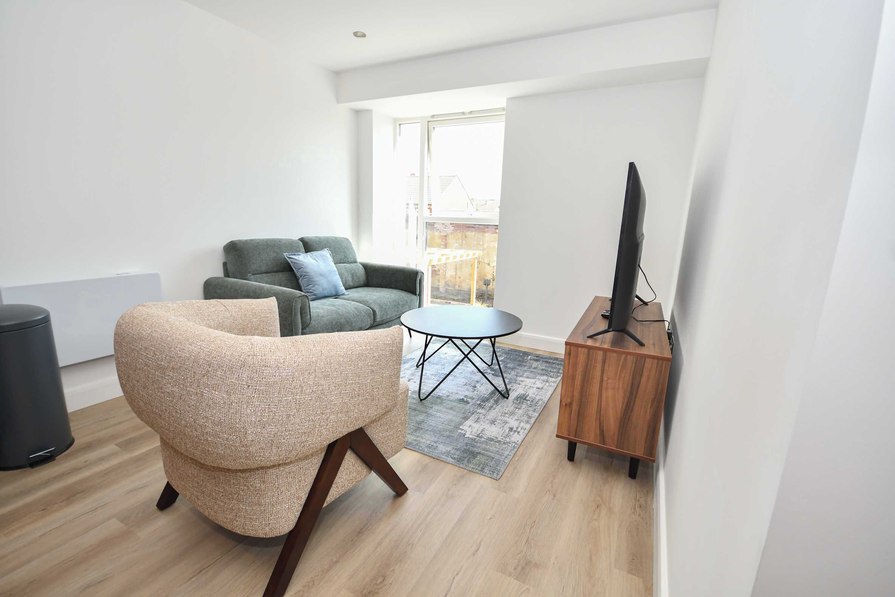 En stue med sofa, lænestol, lille bord, TV-møbel og et vindue.
