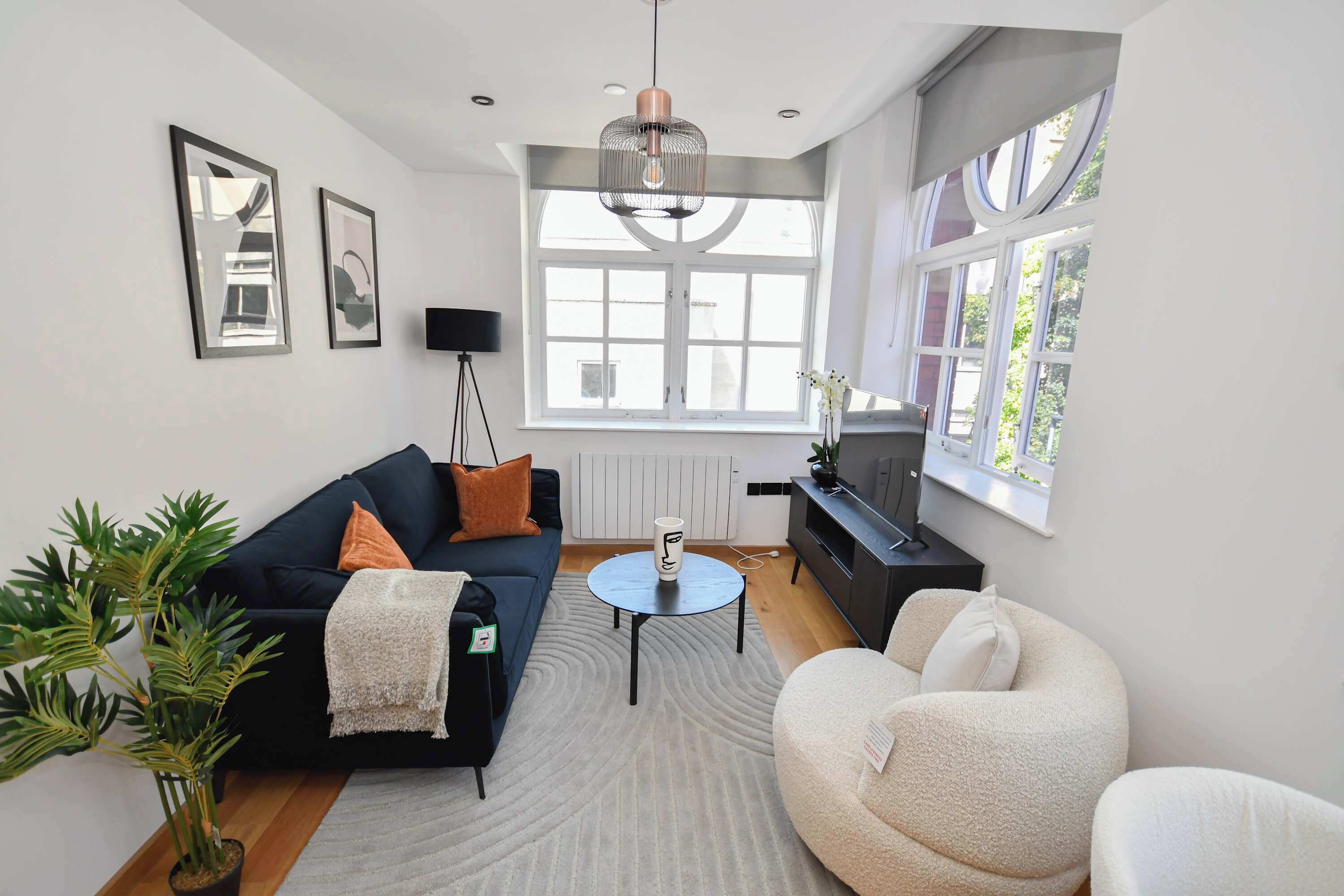 A modern living room with a dark sofa, a round coffee table, a white armchair, a large window, and a potted plant.