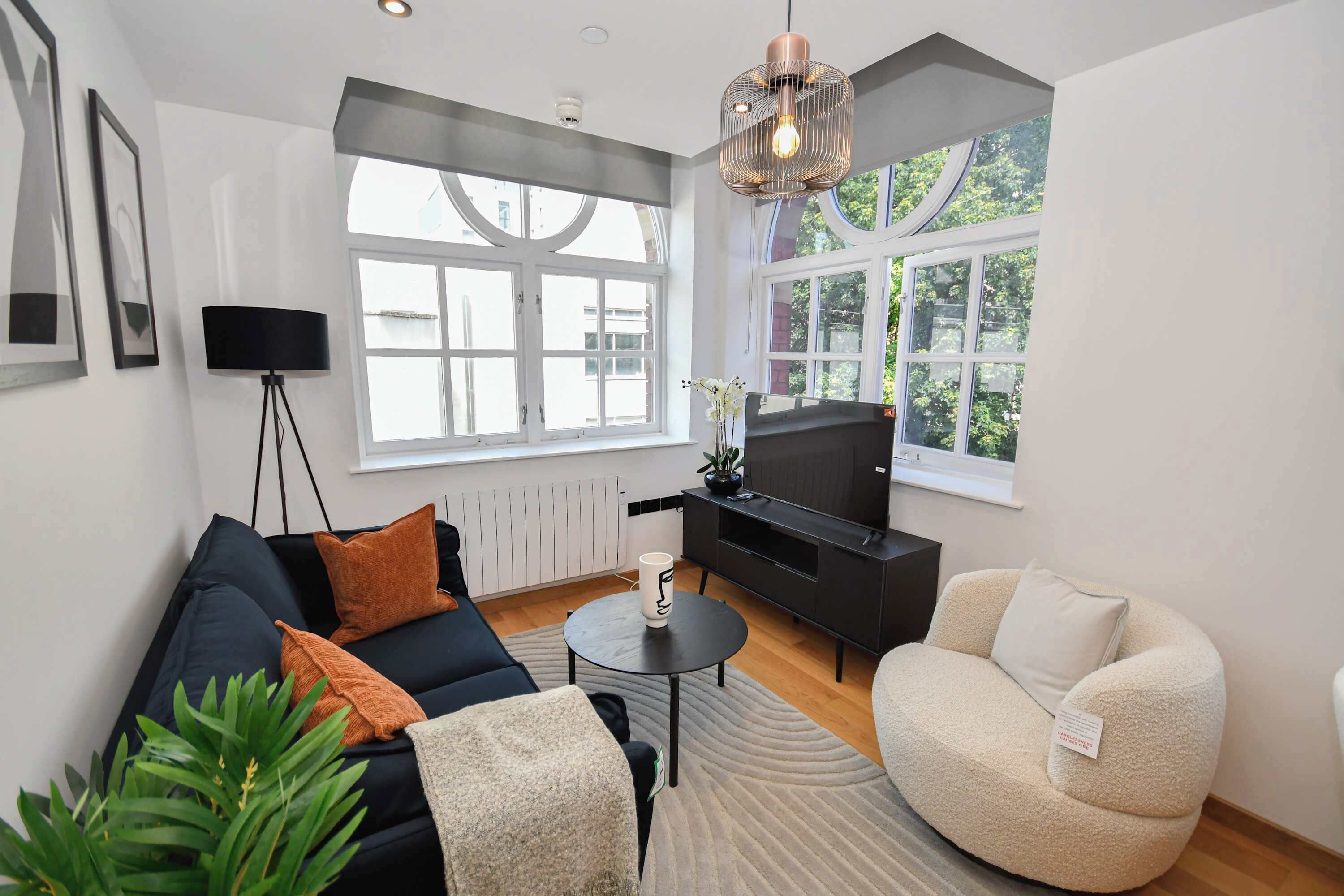 A modern living room with a sofa, armchair, TV stand, and large windows.