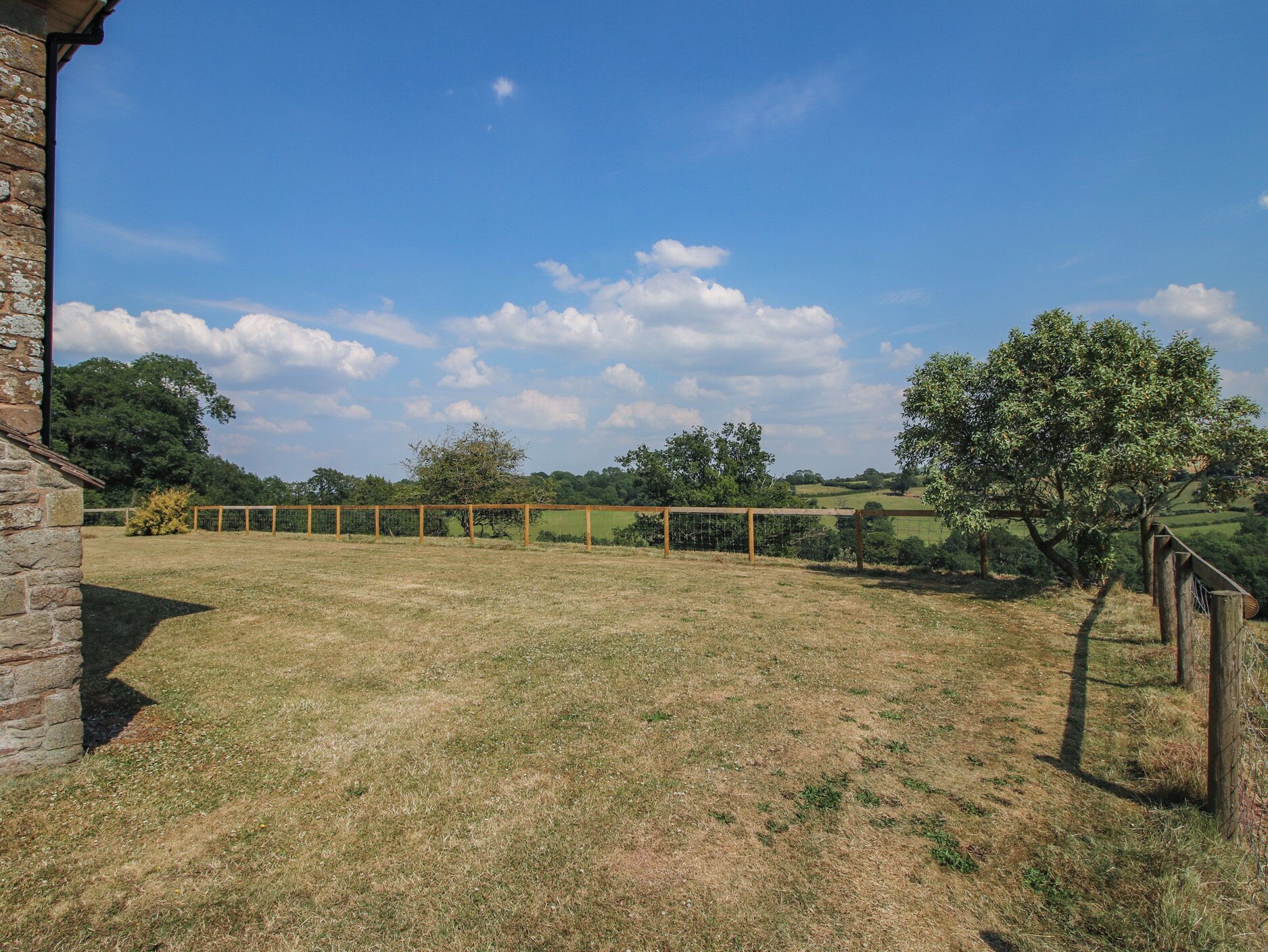 A grassy field with a wooden fence, trees, and a clear sky.