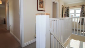 A hallway with a white railing, a framed picture on the wall, and a window with curtains.