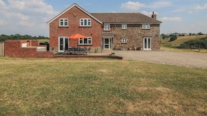 A two-story house with a brick and stone exterior, a front porch with outdoor furniture, and a gravel driveway.