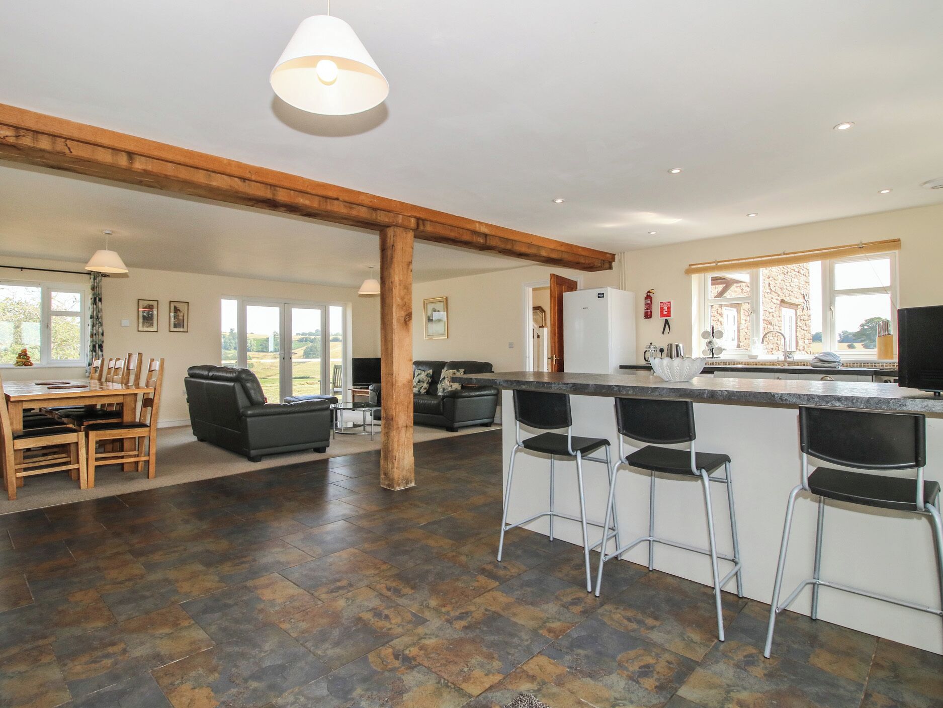 A spacious kitchen with a bar area, wooden beams, and a view of the outdoors.