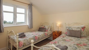 A bedroom with two single beds, a bedside table with a lamp, a window with curtains, and a view of the outdoors.
