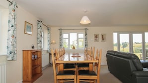 A dining area with a wooden table and chairs, a black leather sofa, and a view of the outdoors through large windows.
