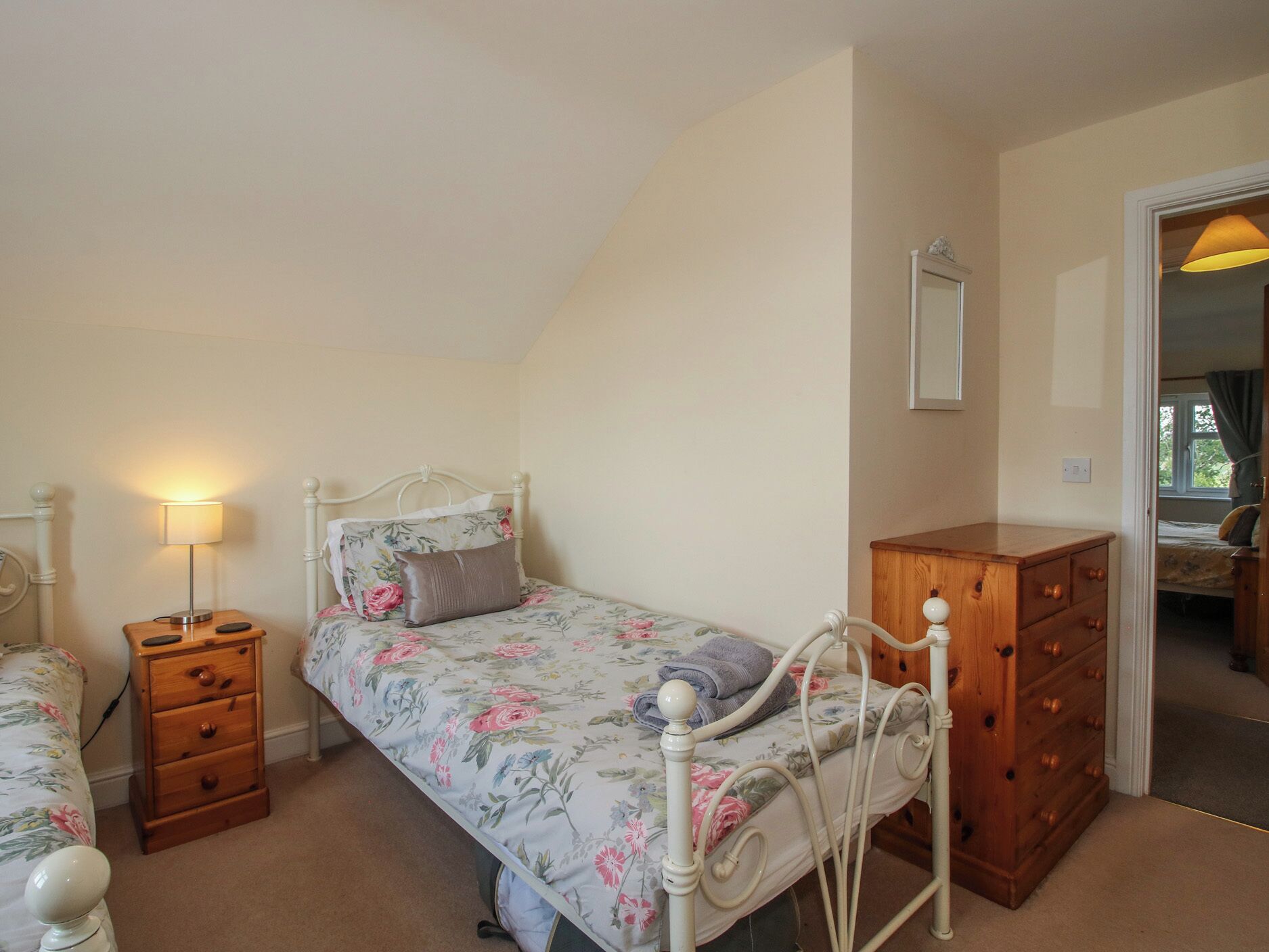 A bedroom with a single bed, a wooden dresser, a nightstand with a lamp, and a mirror on the wall.