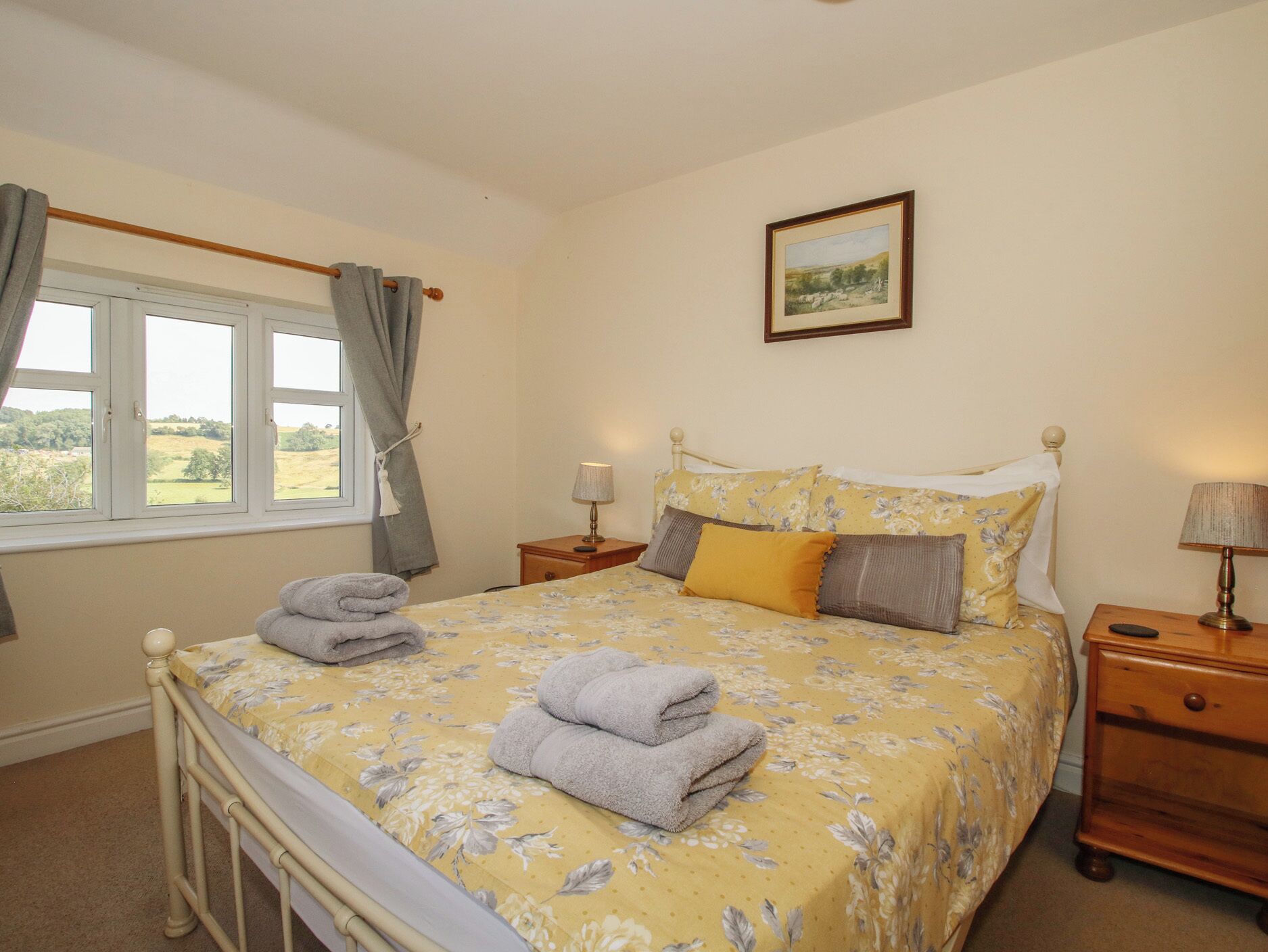 A bedroom with a bed, a nightstand, a lamp, a window with curtains, and a framed picture on the wall.