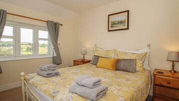 A bedroom with a bed, a nightstand, a lamp, a window with curtains, and a framed picture on the wall.