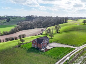 A rural house with a fenced yard, surrounded by green fields and trees. - Wood Cottage (Tenbury Wells)