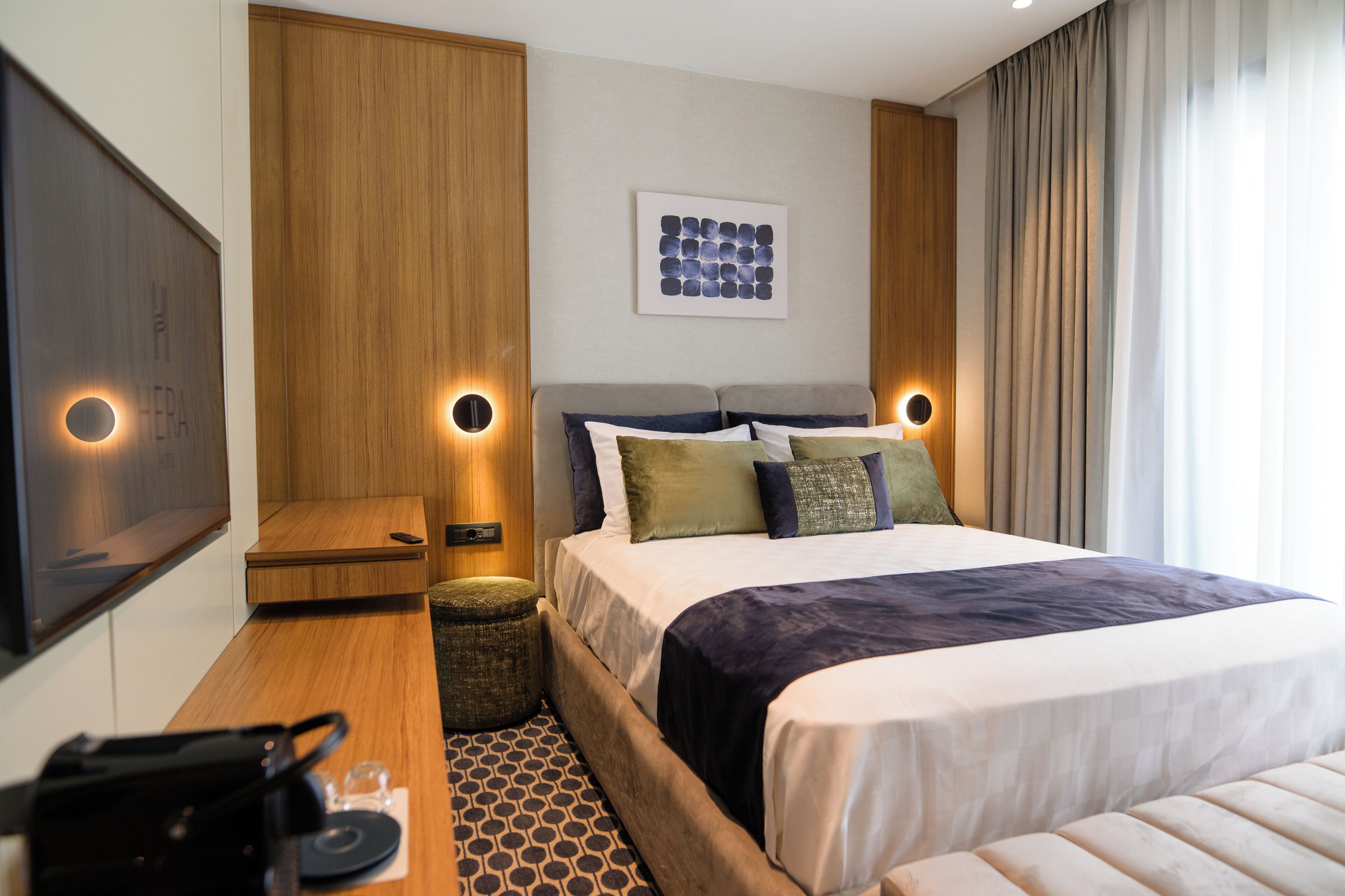Una habitación de hotel moderna con una cama grande, dos mesitas de noche, un televisor de pantalla plana y una obra de arte colgada en la pared.