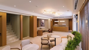 A modern hotel lobby with a reception desk, seating area, and a staircase. - Hera Hotel Axd (Alexandroupoli)