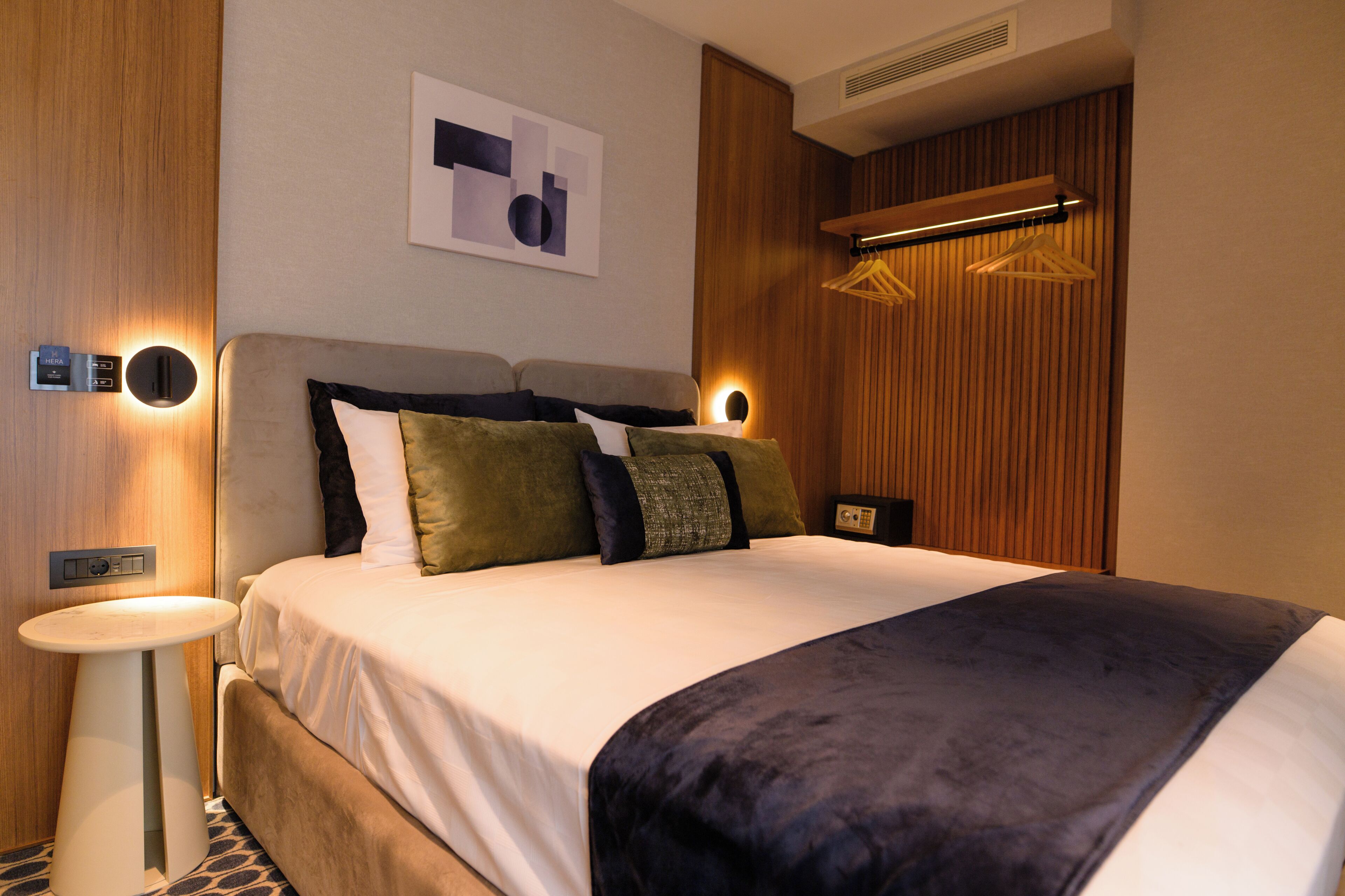 Una habitación de hotel moderna con una cama grande, mesitas de noche, una obra de arte en la pared y un revestimiento de pared de madera.