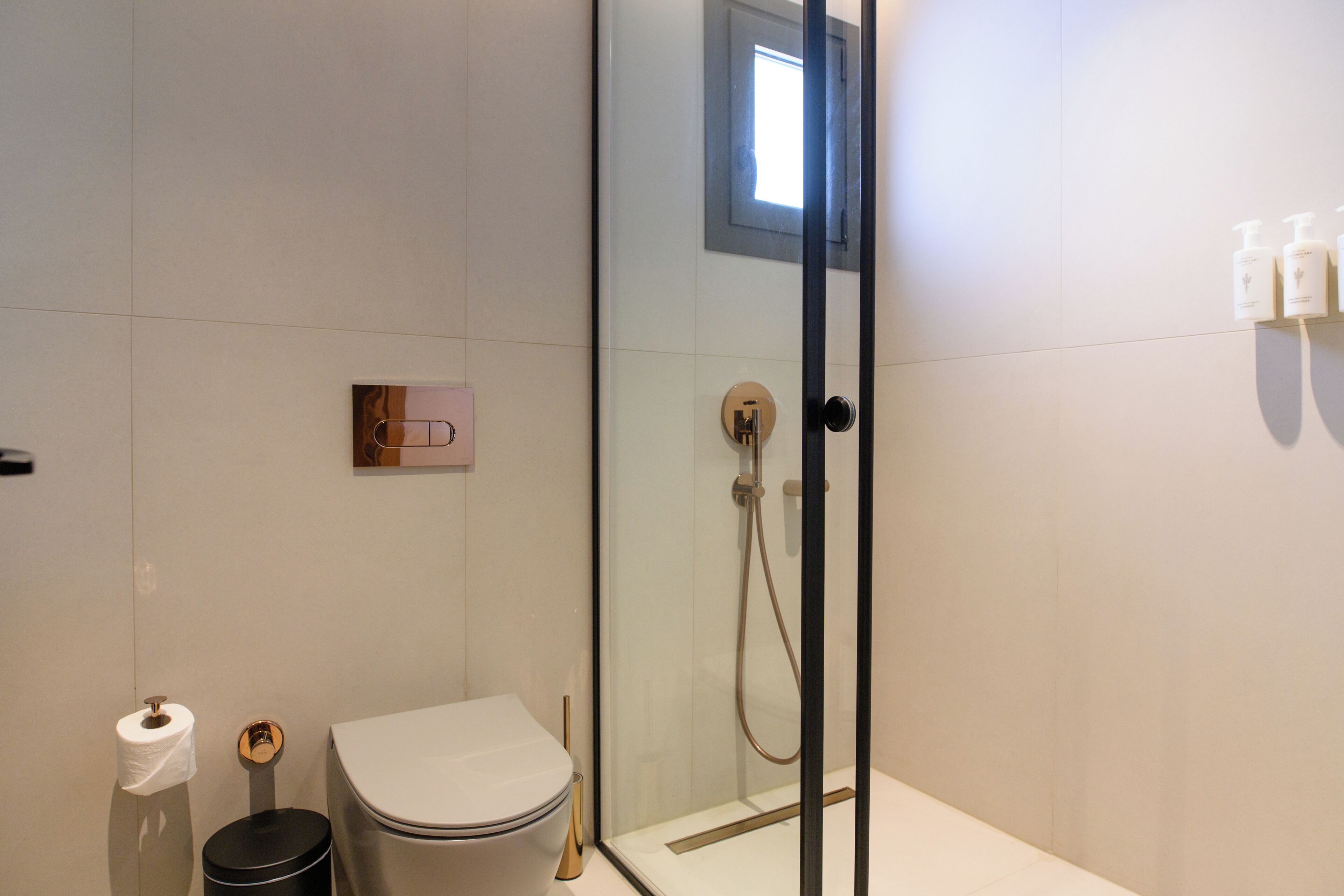 A modern bathroom with a glass-enclosed shower, a toilet, and a trash bin.