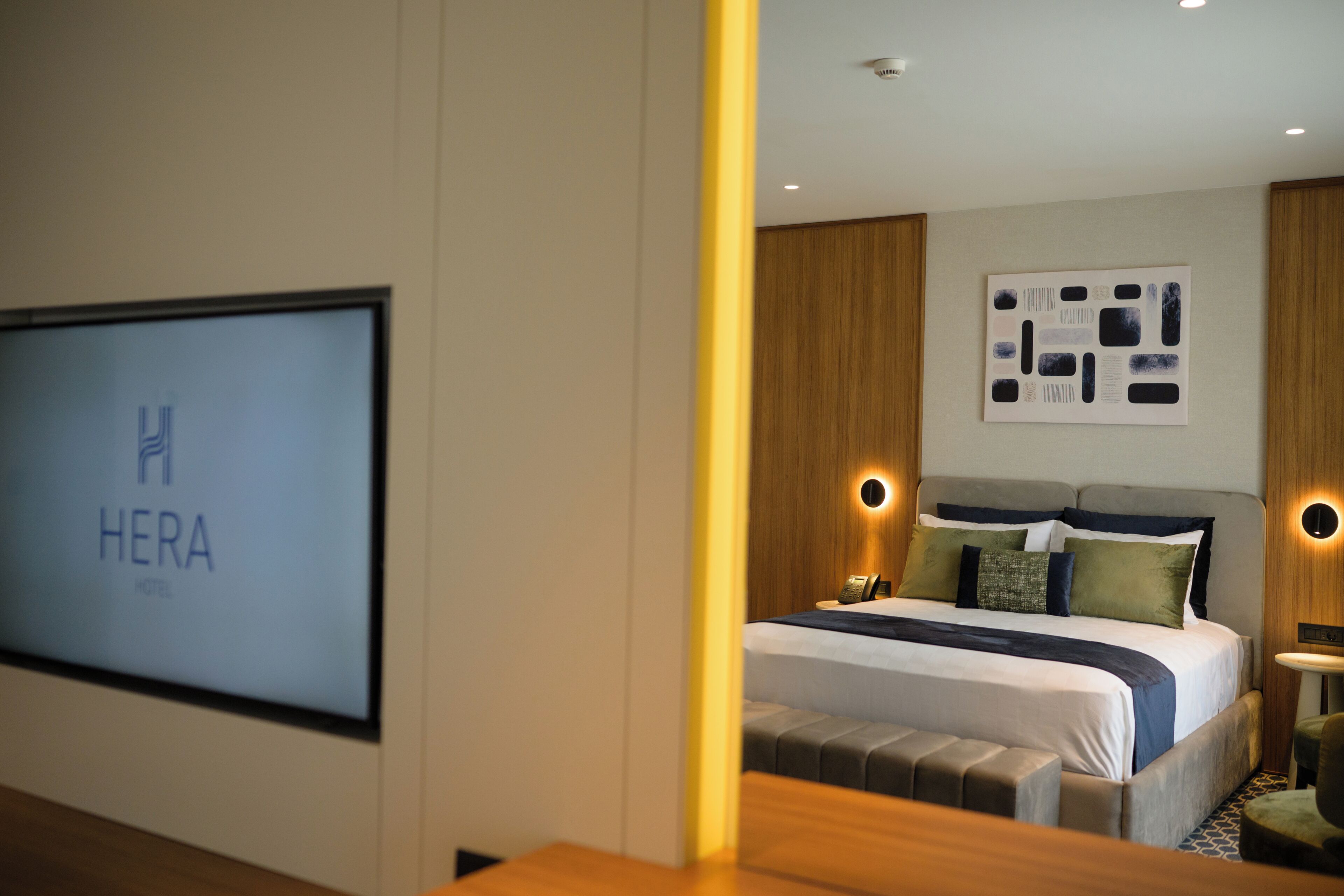 A hotel room with a bed, a wall-mounted TV, and a wooden accent wall.