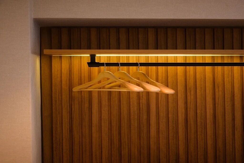 Pared de paneles de madera con una tira de luz horizontal y una barra de metal que sostiene tres perchas de madera.