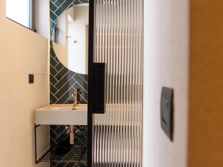 A modern bathroom with a herringbone tile backsplash, a white sink, and a black-framed mirror.
