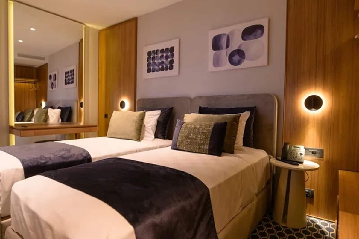 Habitación de hotel con dos camas, una mesita de noche con teléfono, un espejo y una obra de arte en la pared.