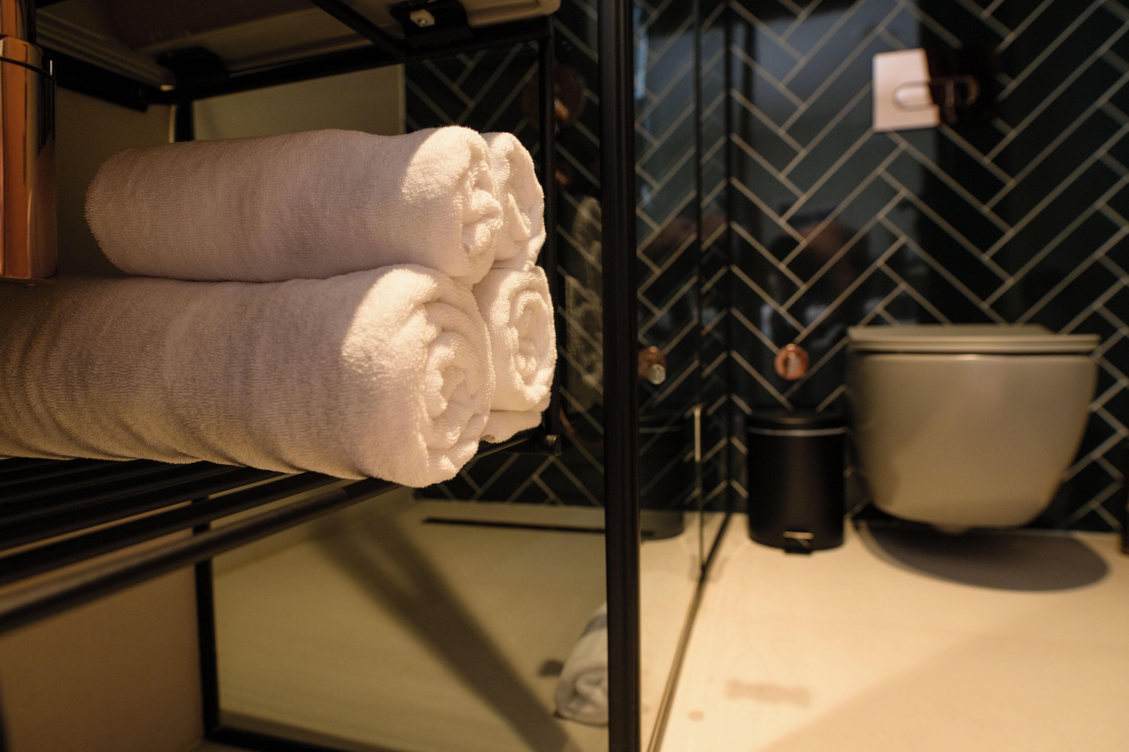 A bathroom with a towel rack holding folded towels, a toilet, and a black trash bin.