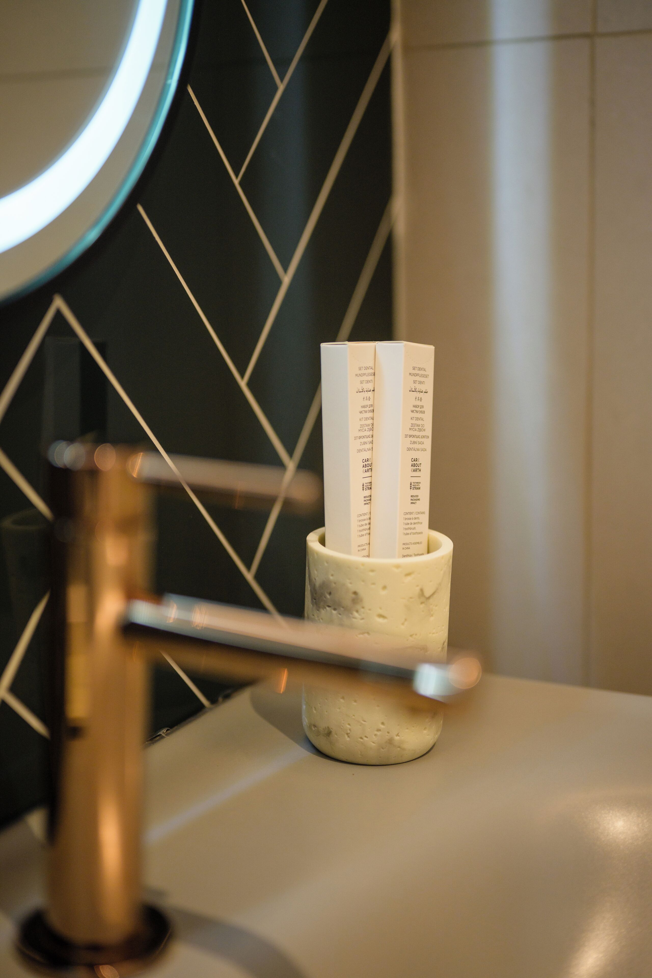 A bathroom with a sink, a cup holding rolled-up papers, and a wall with a geometric pattern.