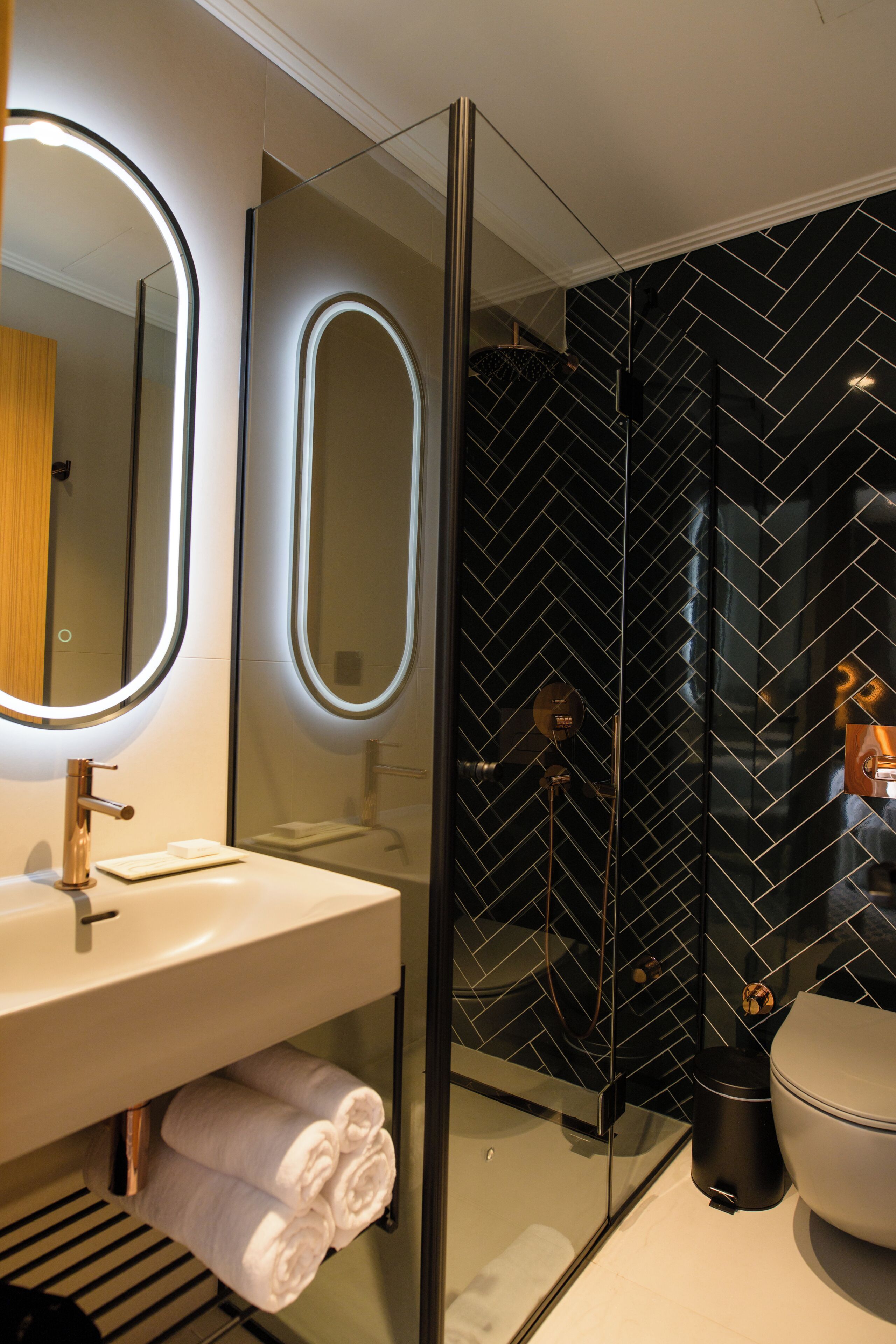 Un baño moderno con ducha envuelta en cristal, un lavabo blanco e iluminación integrada en un espejo.