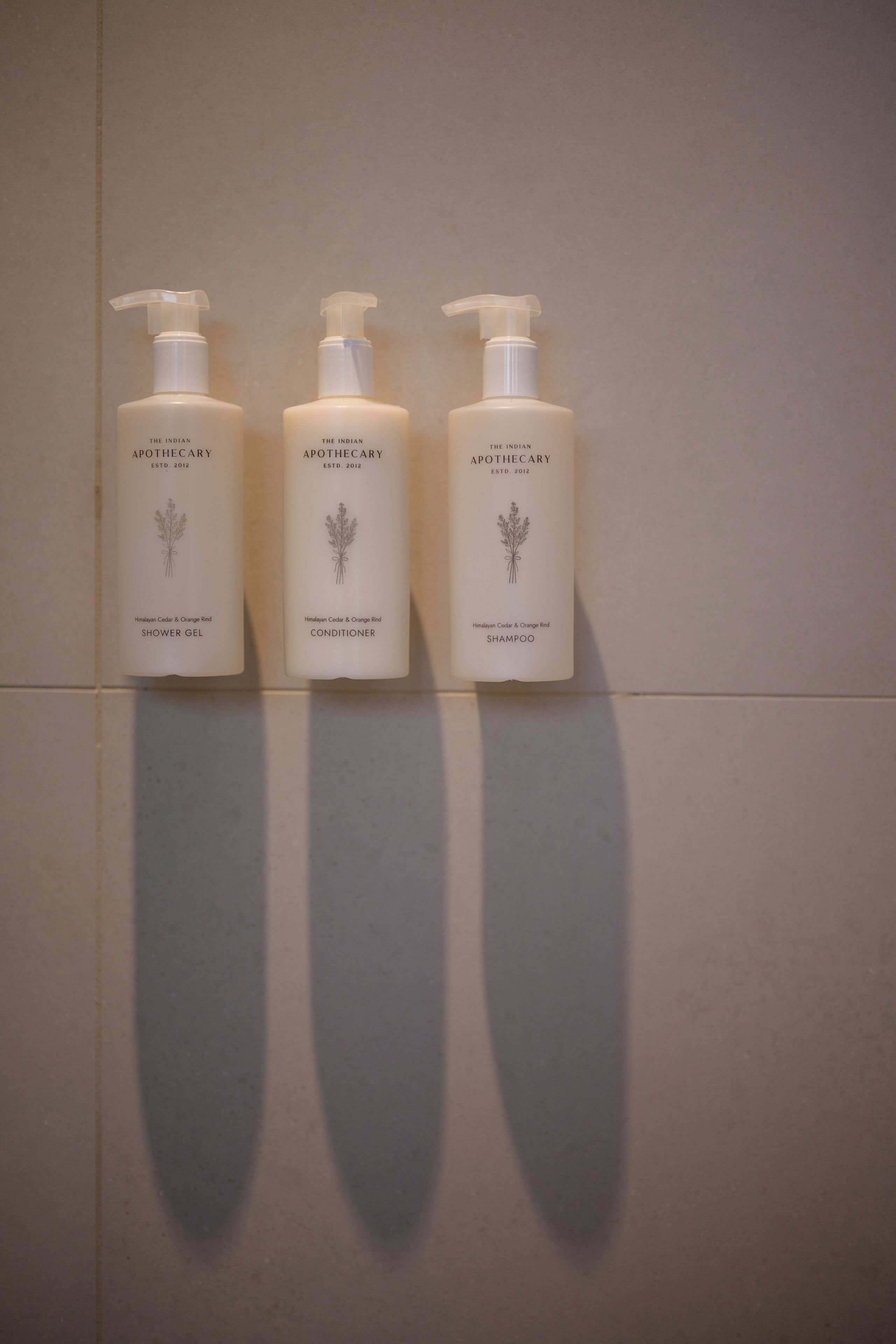 Tre flaconi di prodotti The Indian Apothecary su un muro piastrellato.