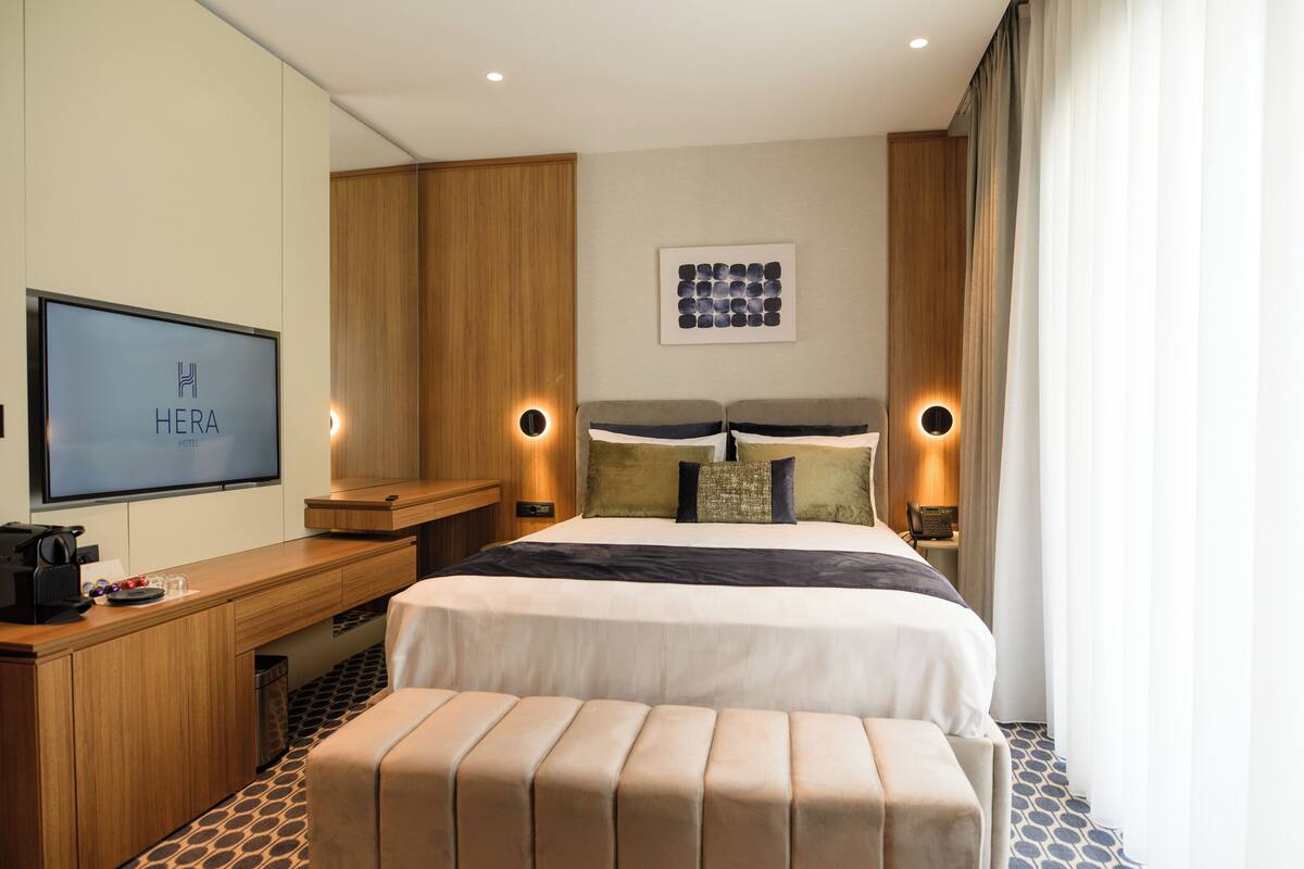 Habitación de hotel con cama, lámparas de noche, escritorio, televisor y una obra de arte colgada en la pared.