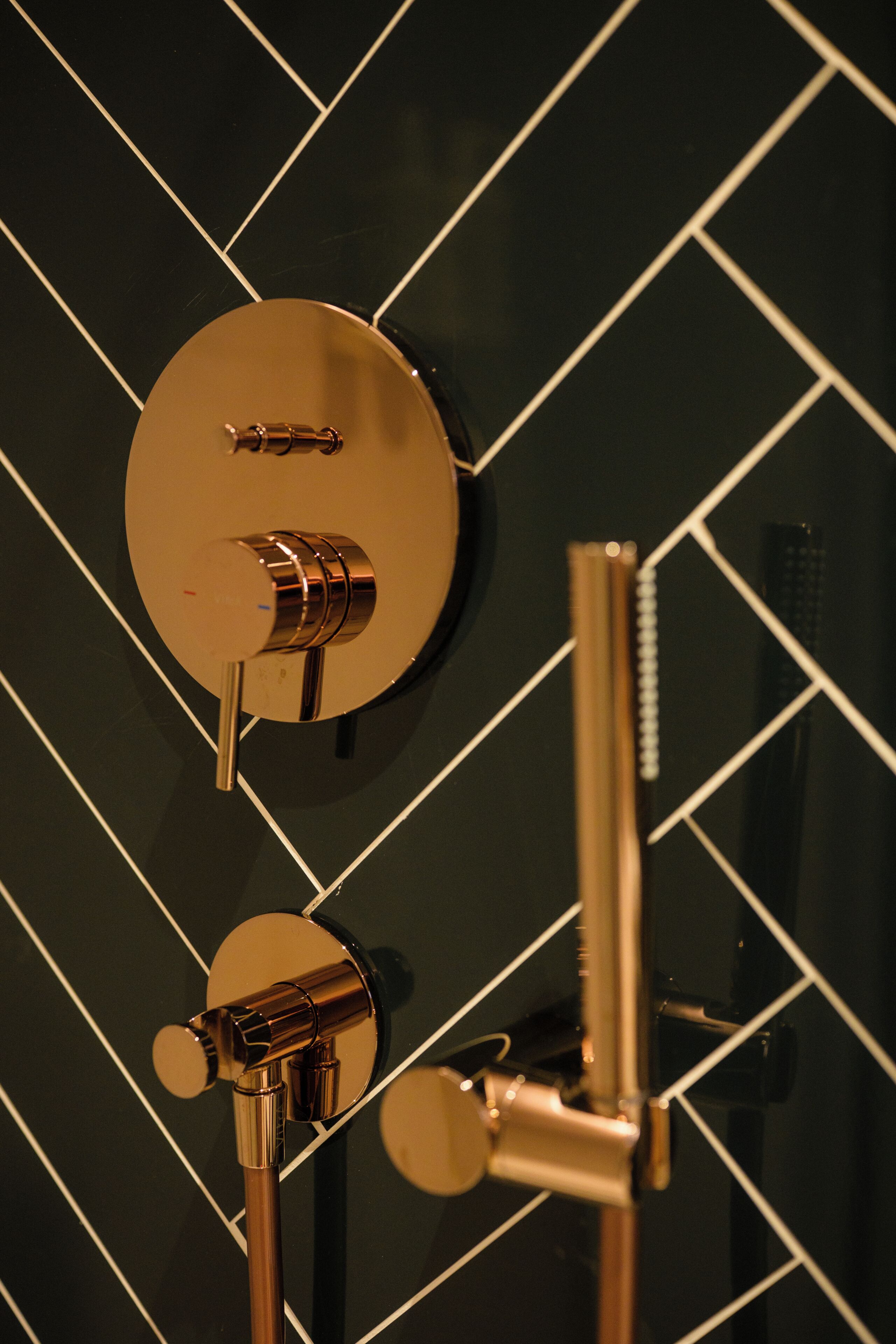 Une salle de bain avec un mur recouvert de carreaux noirs et un panneau de commande doré pour la douche.
