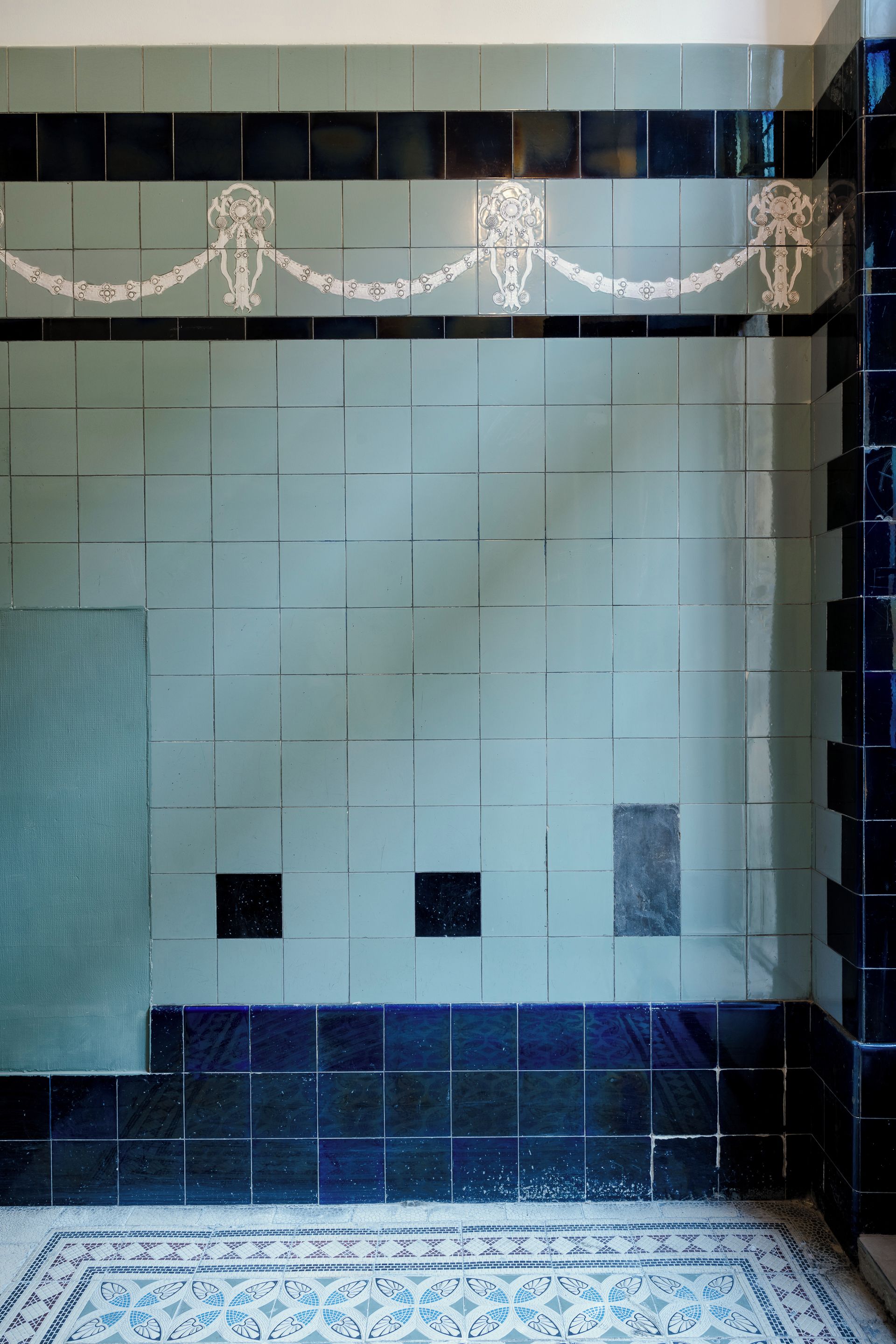 Une salle de bain carrelée, avec un sol à motifs et une bordure décorative au-dessus du lavabo.
