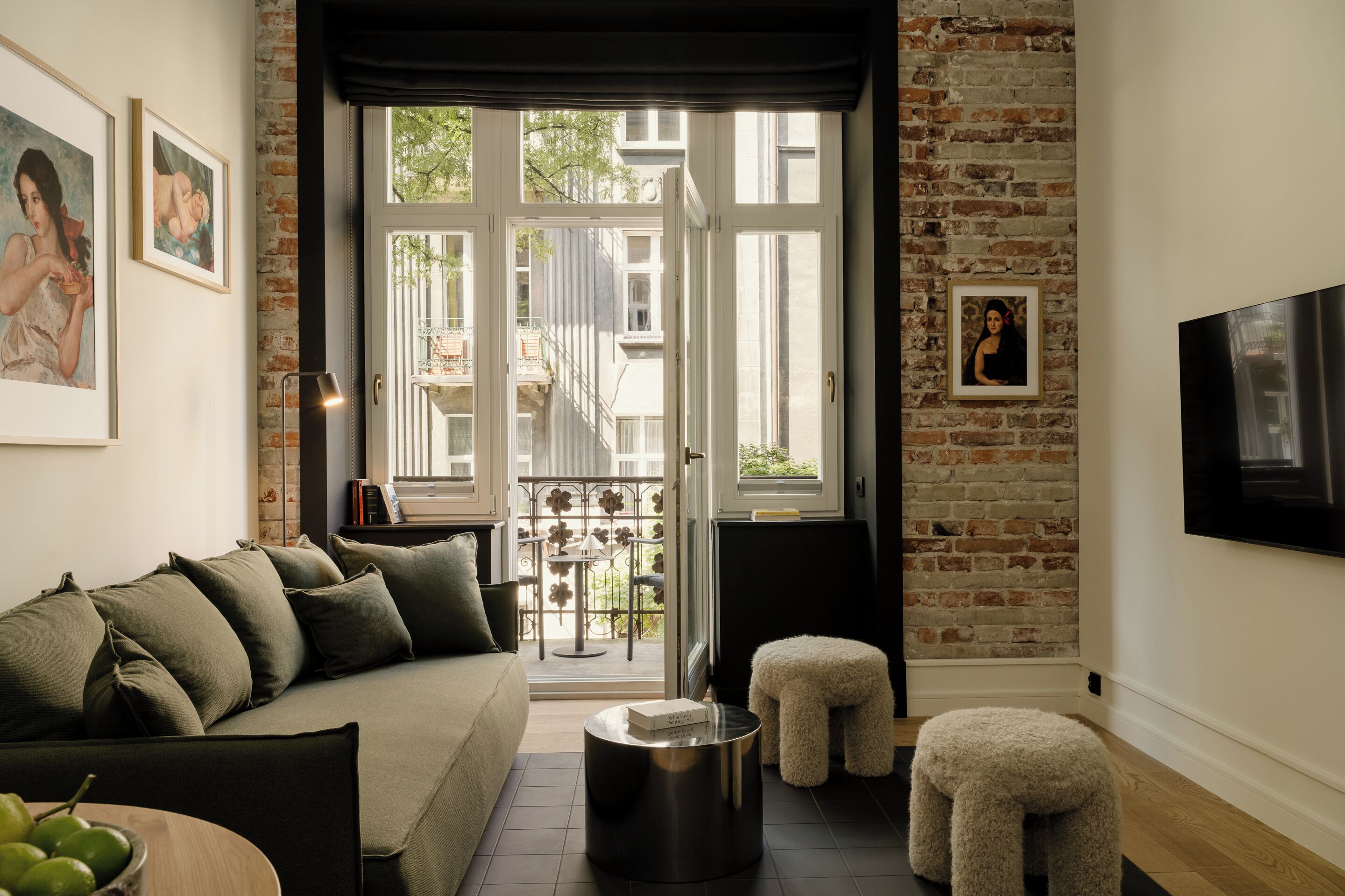 A living room with a sofa, a small round table, a stool, and a TV mounted on the wall.