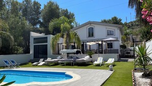 Una casa moderna con piscina, tumbonas y zona de patio.