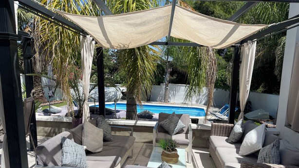 Un área de estar exterior con sofás y sillones, una piscina y una pérgola.