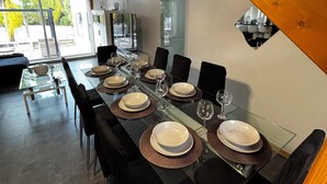 Un comedor con una mesa larga dispuesta para una comida, sillas negras y un diseño moderno en el techo.