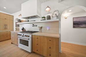 A modern kitchen with a central island, wooden cabinets, and a built-in oven. - Vine Retreat Near Texas A&M (Bryan)