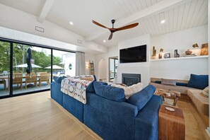 A modern living room with a blue sofa, a flat-screen TV, and a ceiling fan. - Vine Retreat Near Texas A&M (Bryan)
