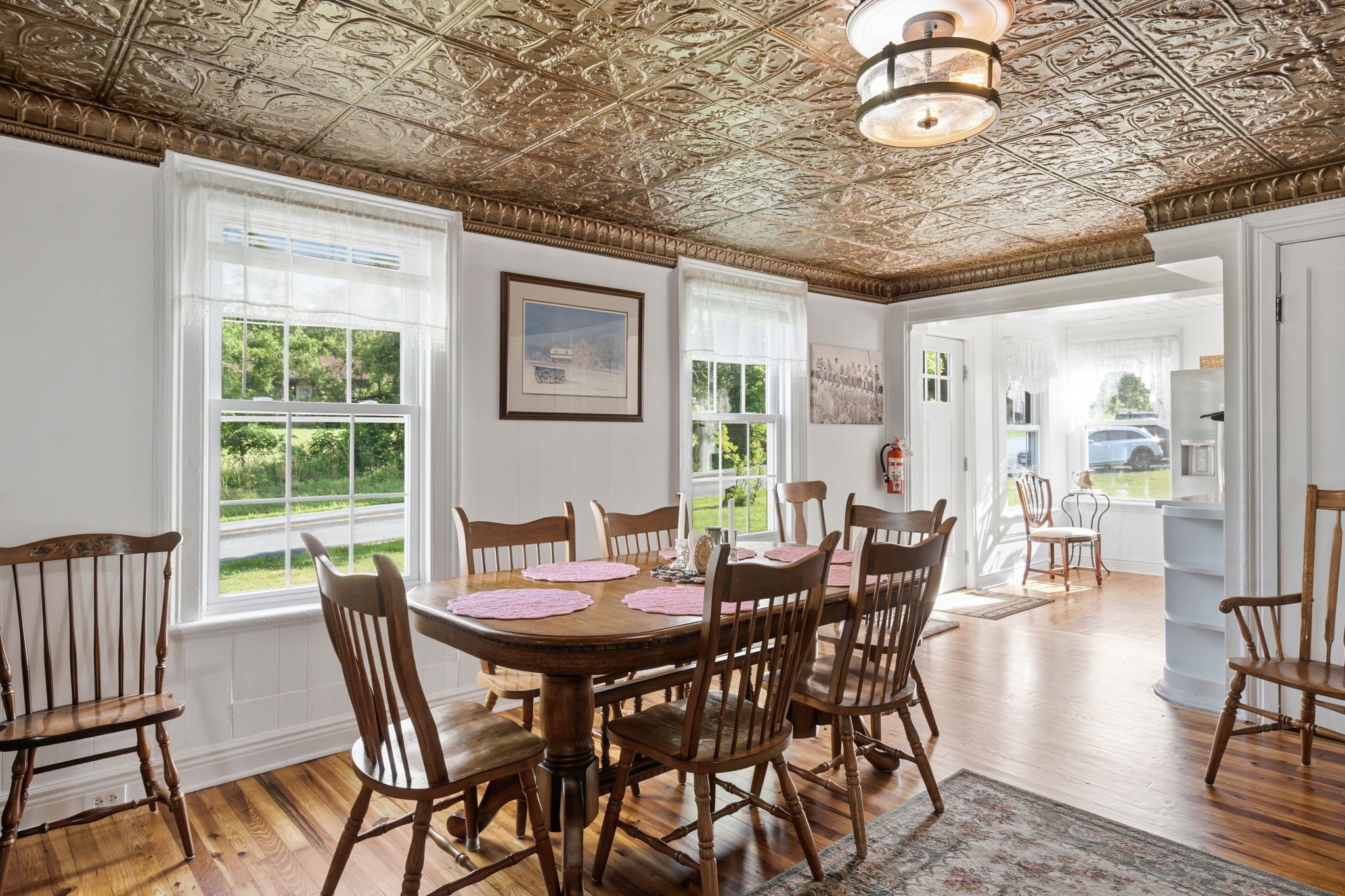 A dining room with a wooden table and chairs, large windows, and a decorative ceiling.