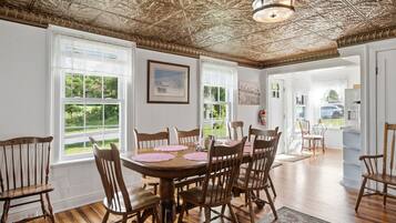 A dining room with a wooden table and chairs, large windows, and a decorative ceiling.